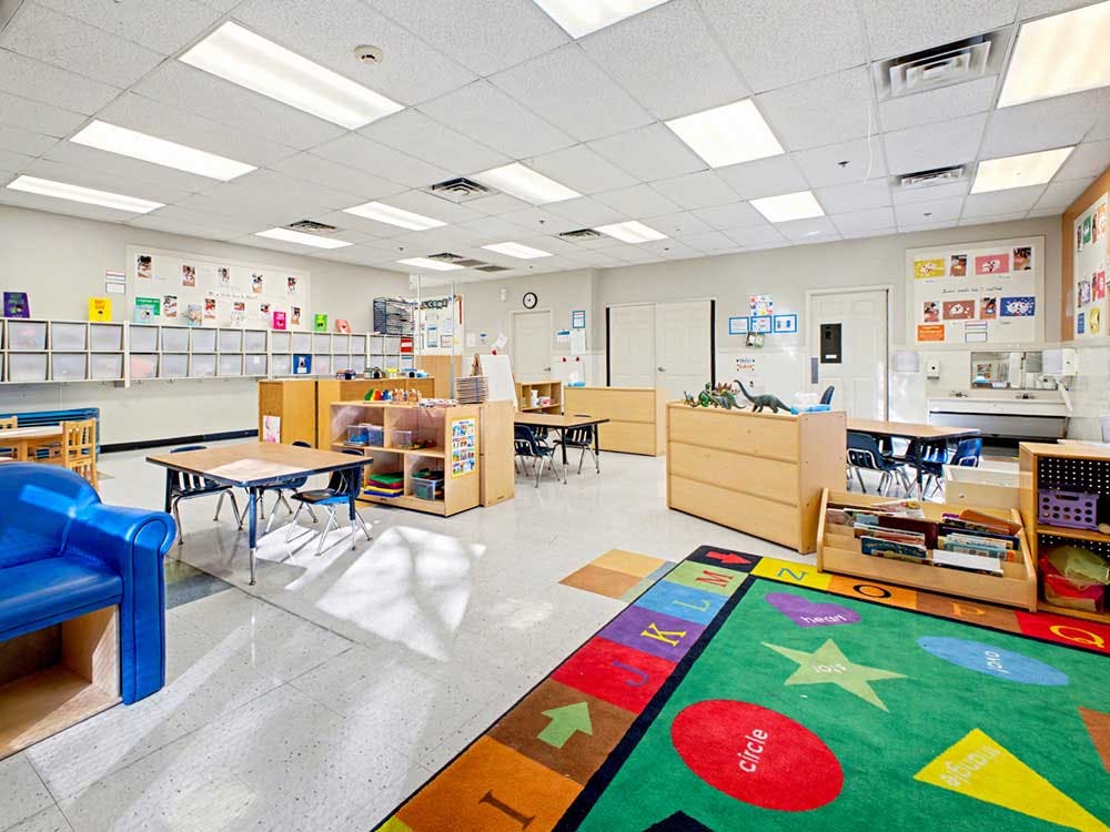 Empty classroom with tables, chairs, storage cubbies, and a colorful rug