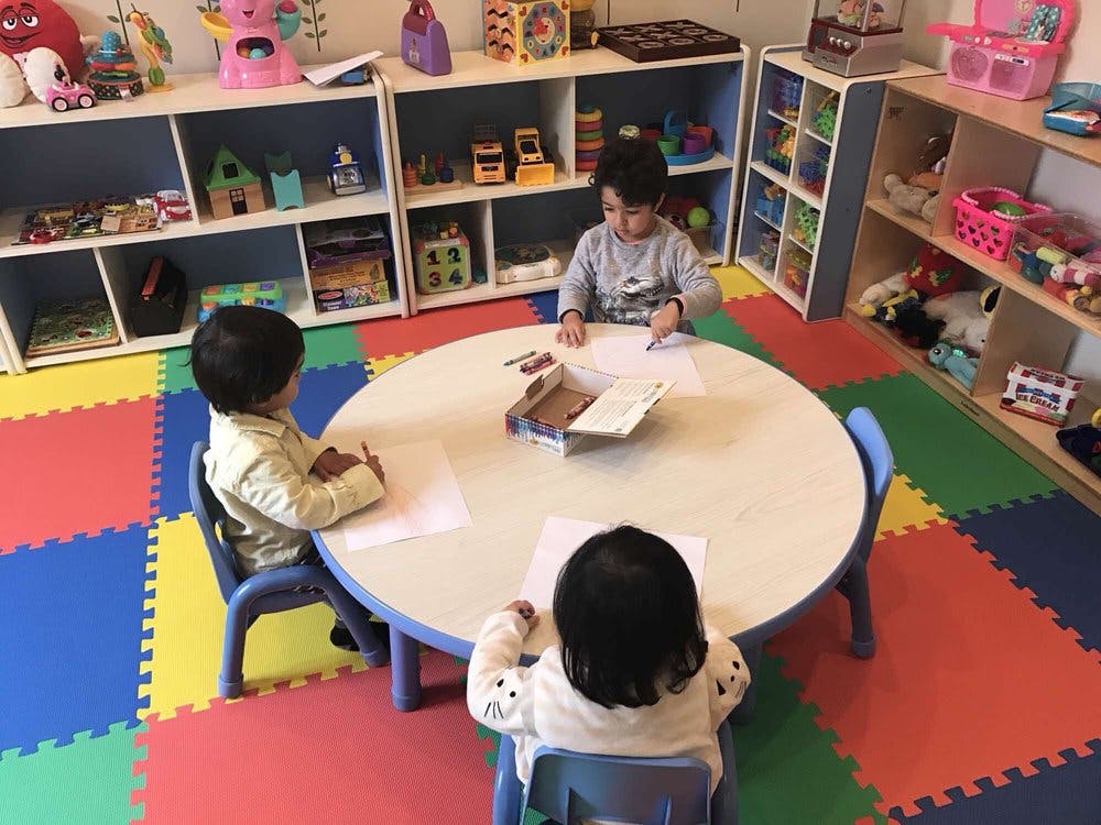 Three children drawing at a round table in a classroom