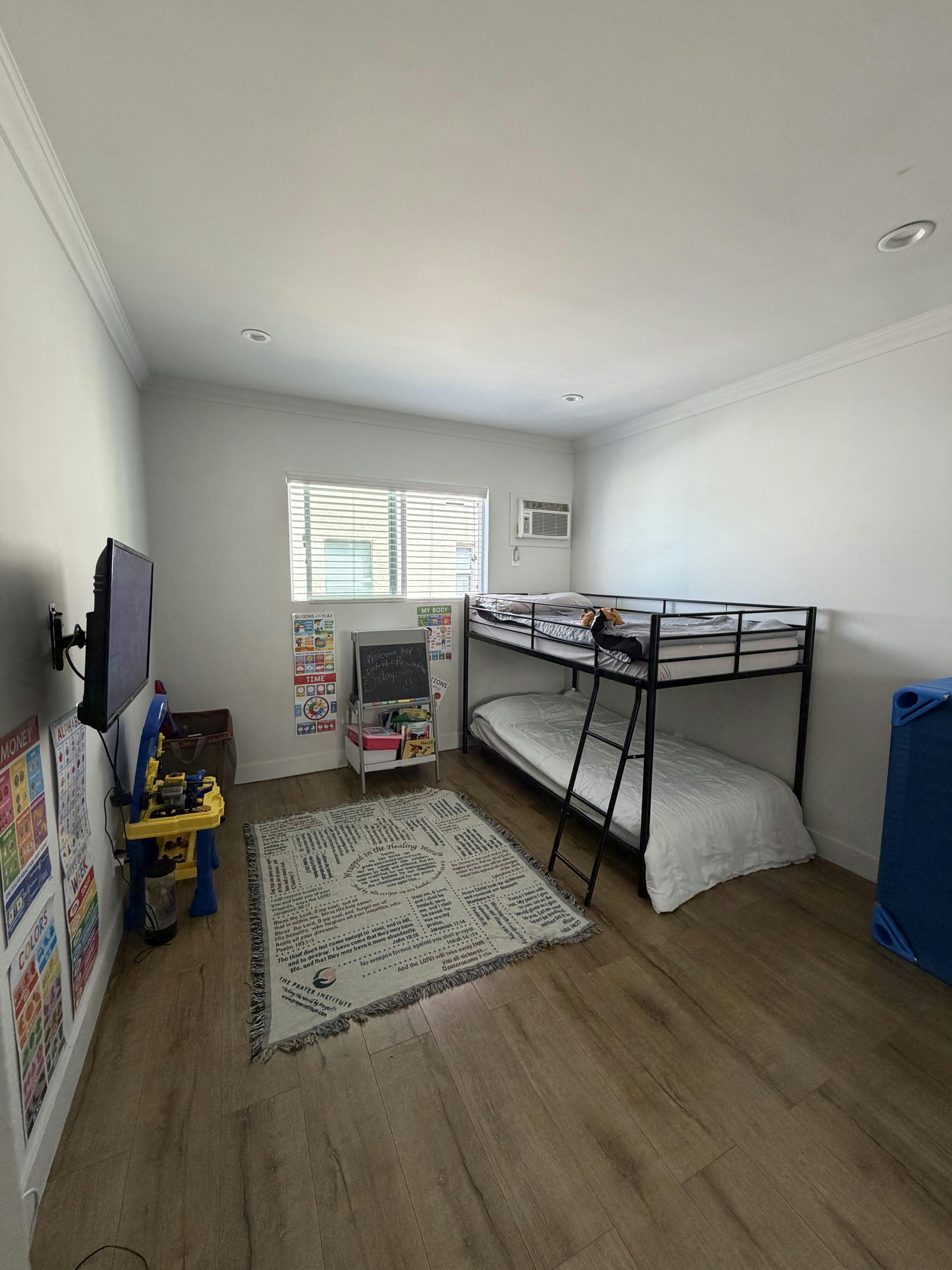 Child's bedroom with a black metal bunk bed, window with blinds, and white walls