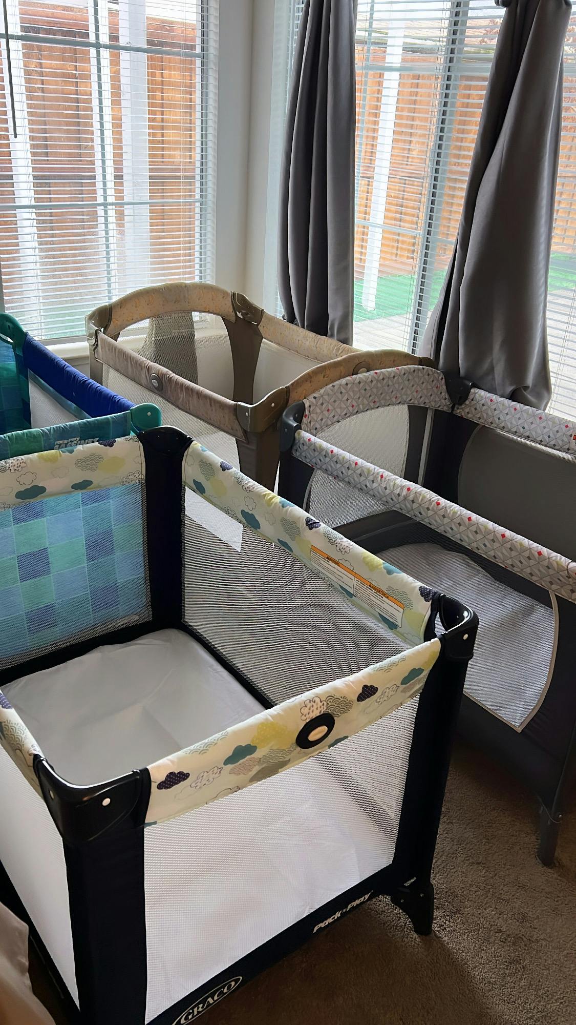 Multiple baby cribs and playards in a room with windows