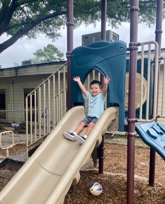Child on a playground slide with arms raised