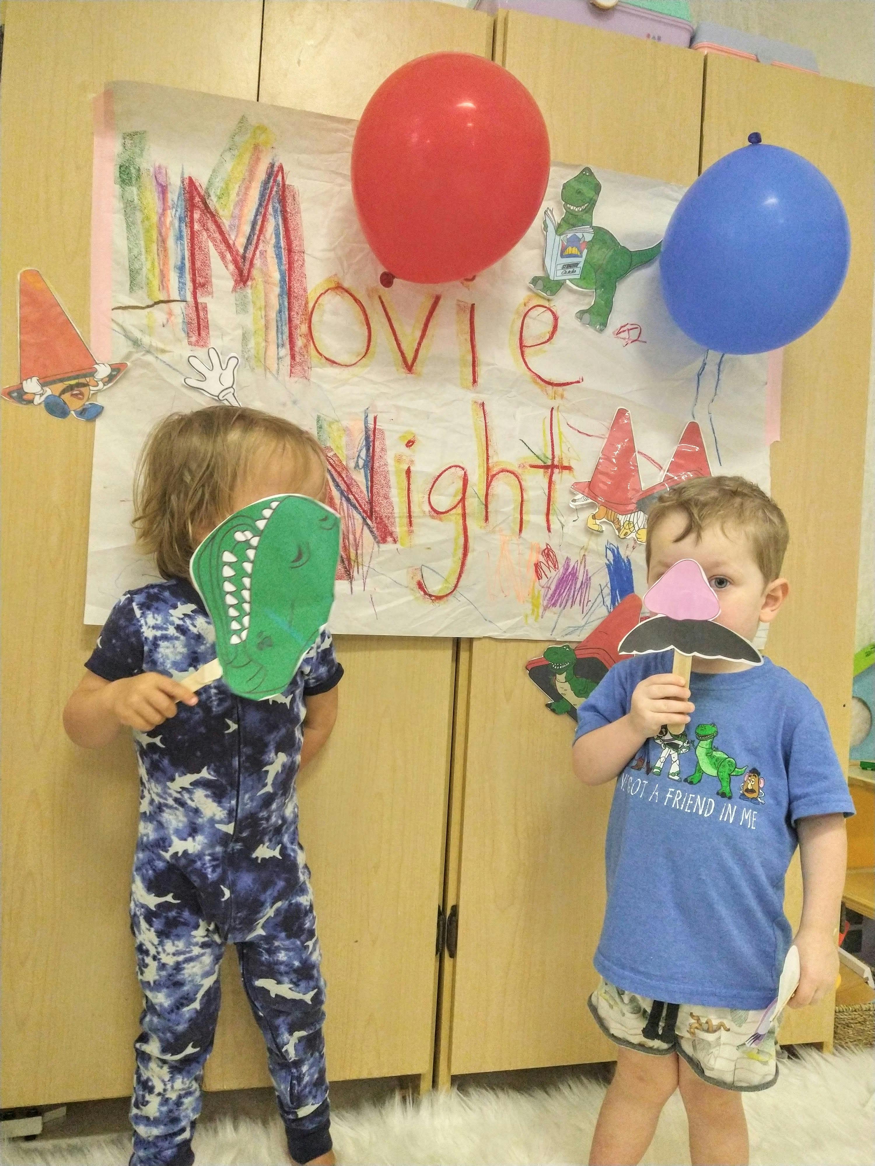 Two children holding up props in front of a "Movie Night" sign