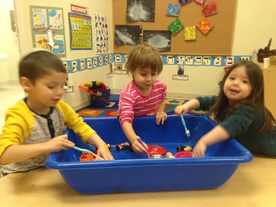 Three children playing with toys in a blue bin in a classroom
