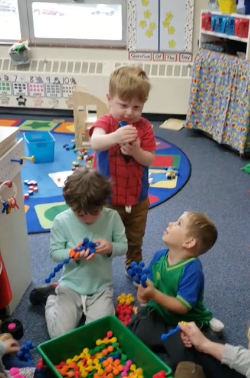 Three children playing with colorful building toys in a classroom