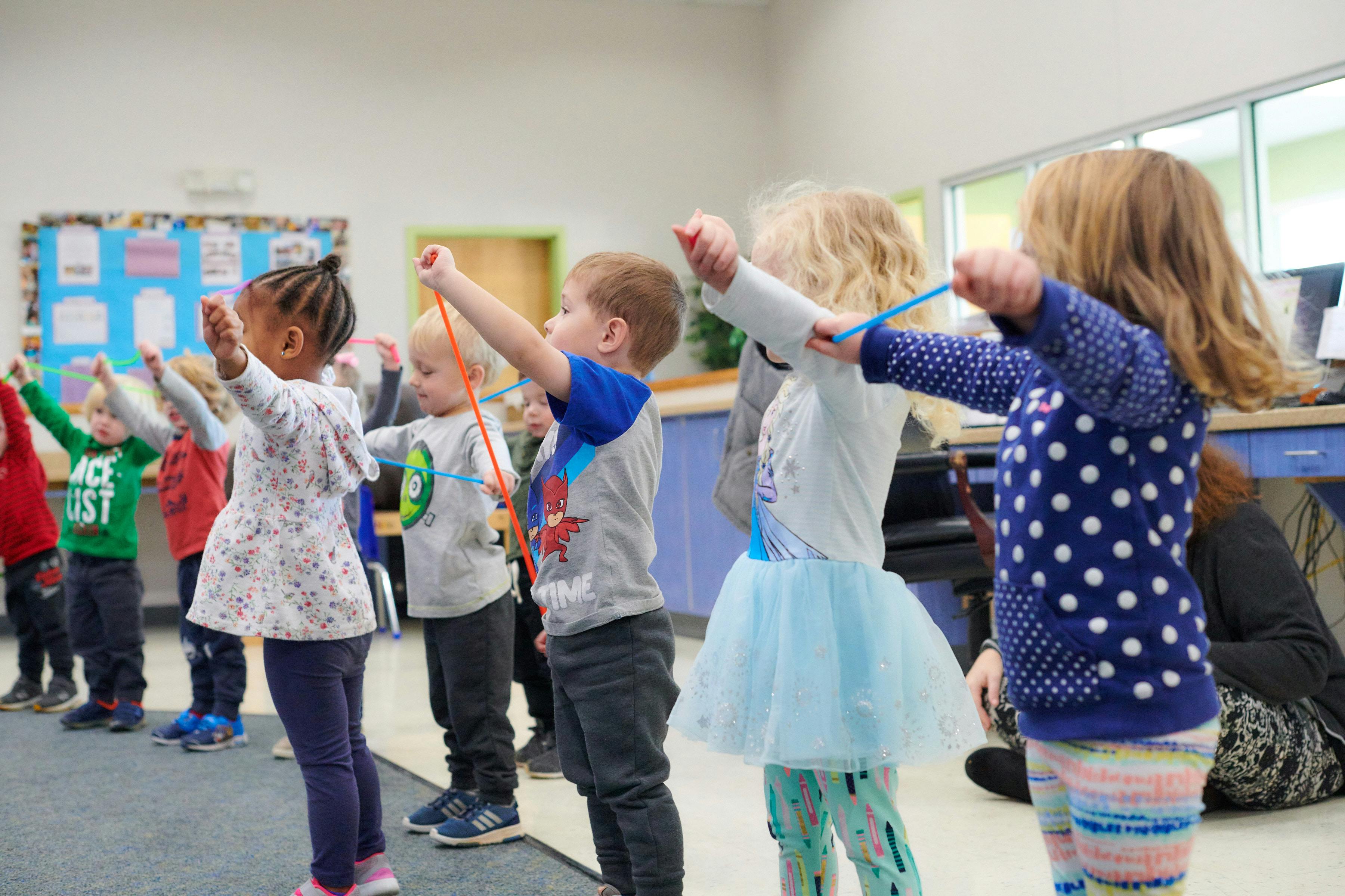Children standing in a line with arms raised, holding colorful objects