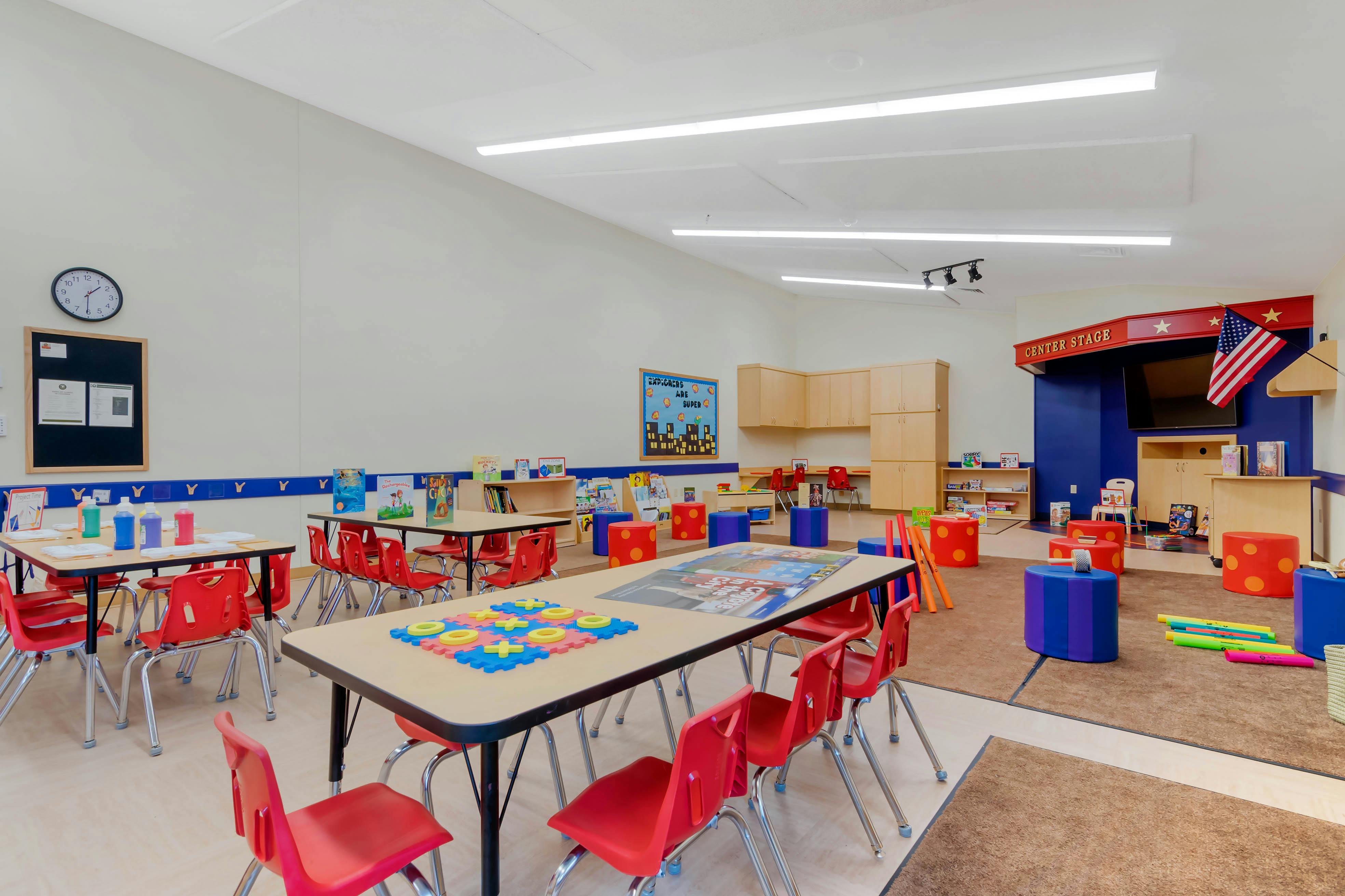 Classroom with small tables, red chairs, and a stage area with "CENTER STAGE" text