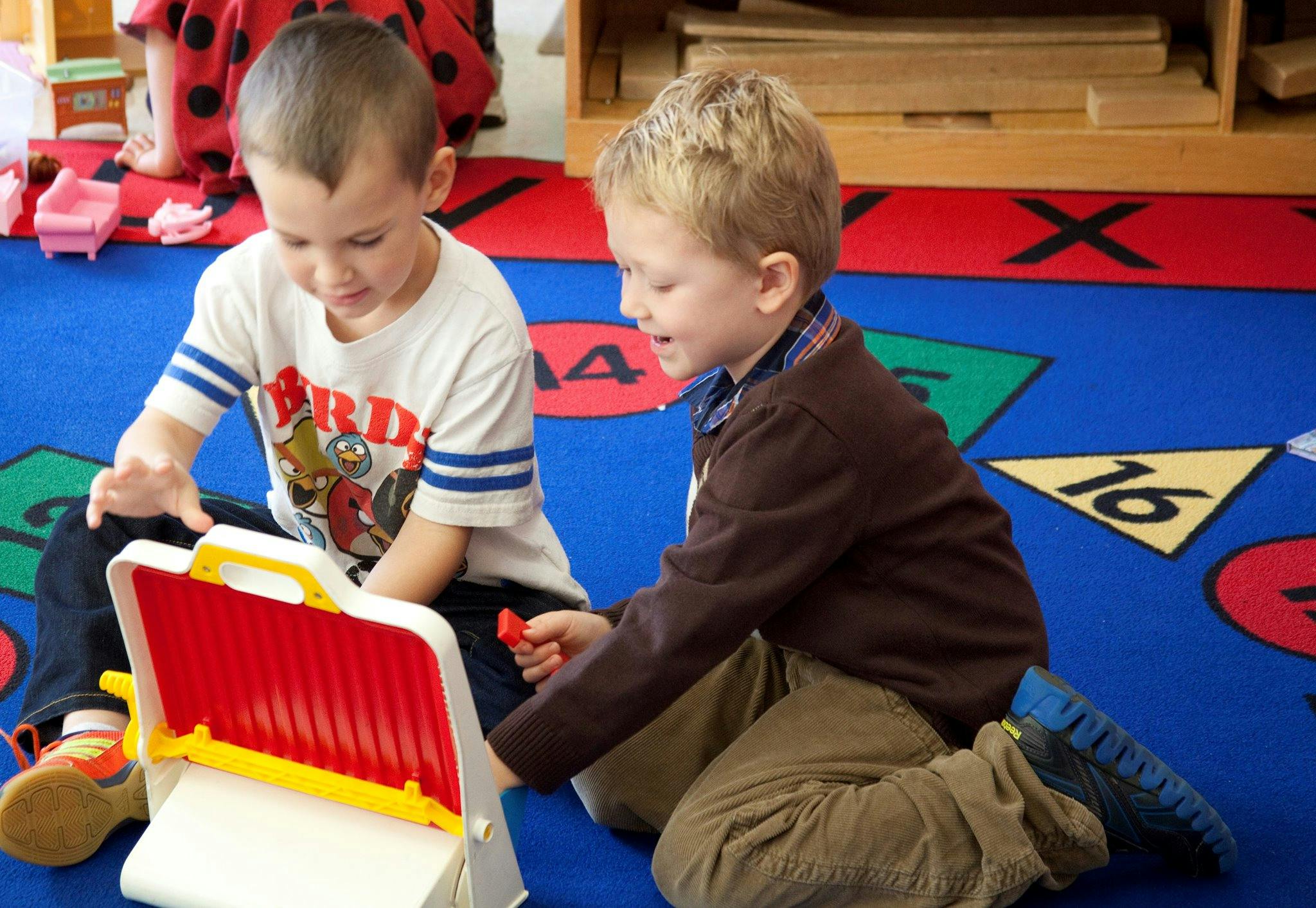Two children playing with a toy on a colorful rug in a classroom