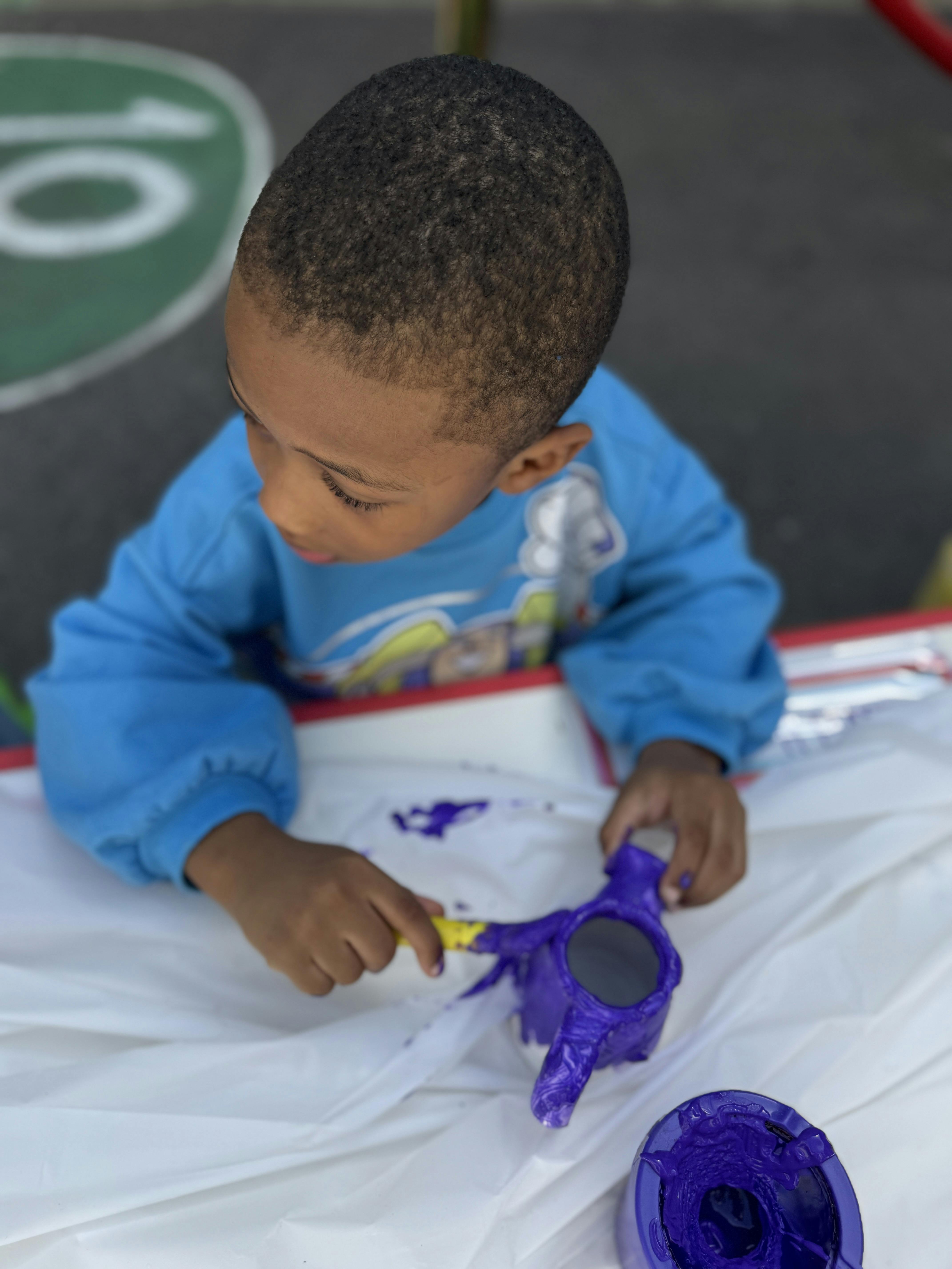 Child painting a purple object with a yellow brush