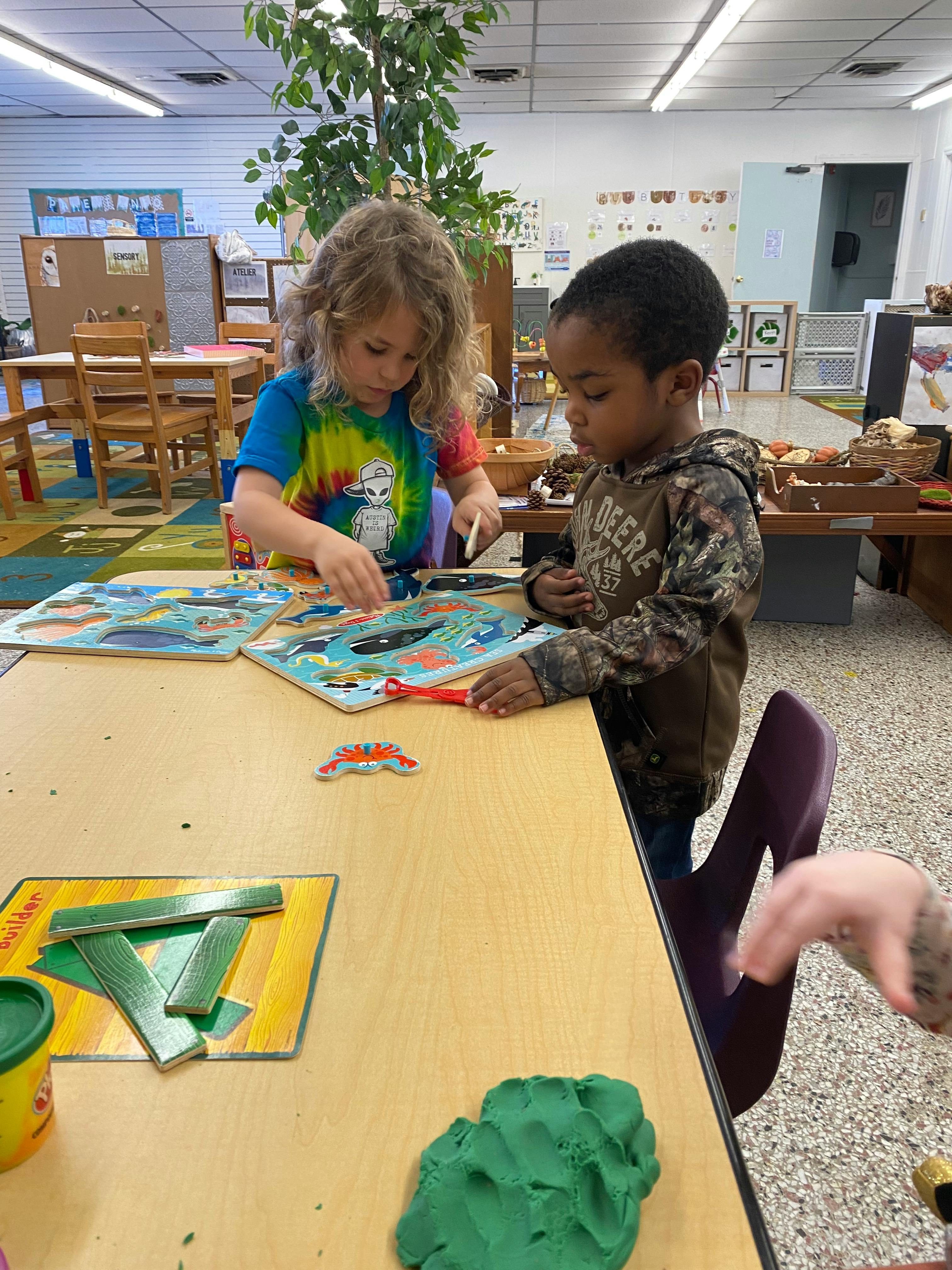 Two children playing with puzzles at a table in a classroom