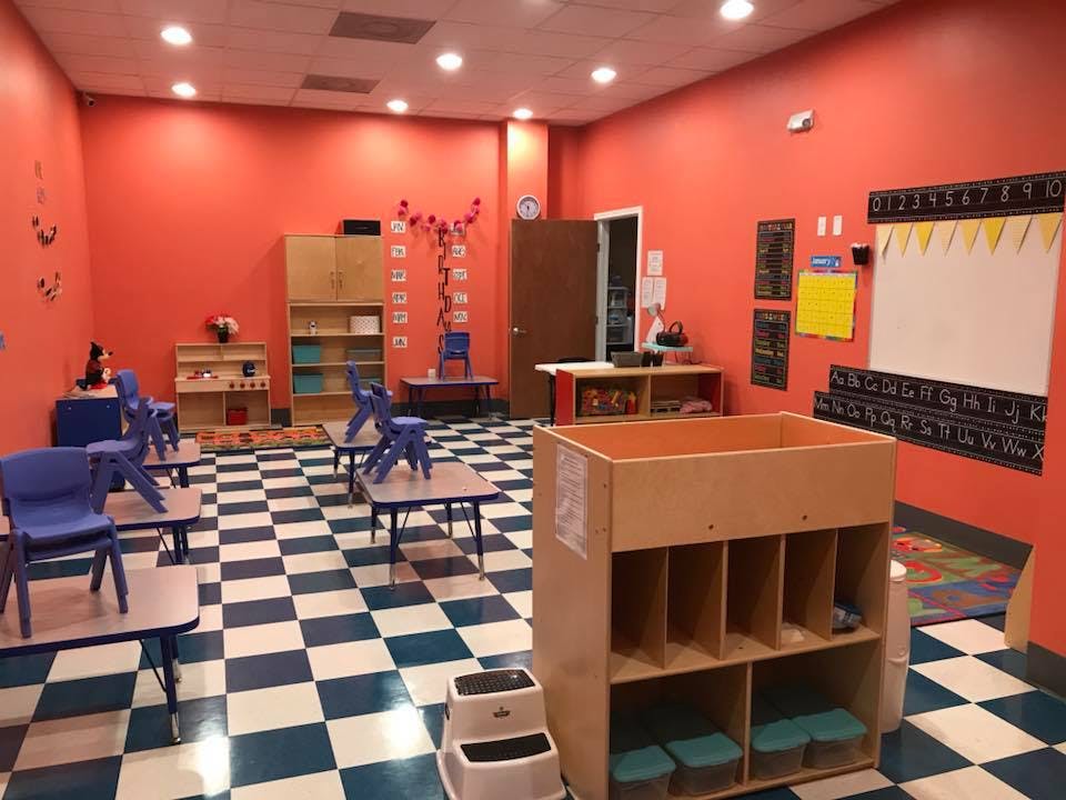 Classroom with small tables and chairs, red walls, and checkered floor