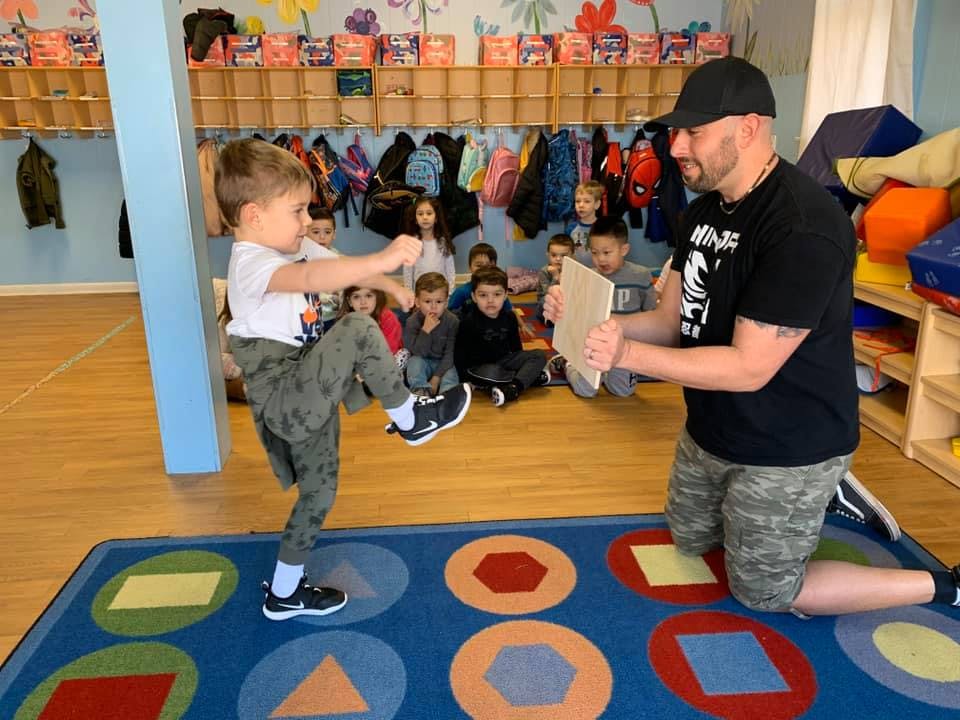 Child kicking a board held by an adult in a classroom