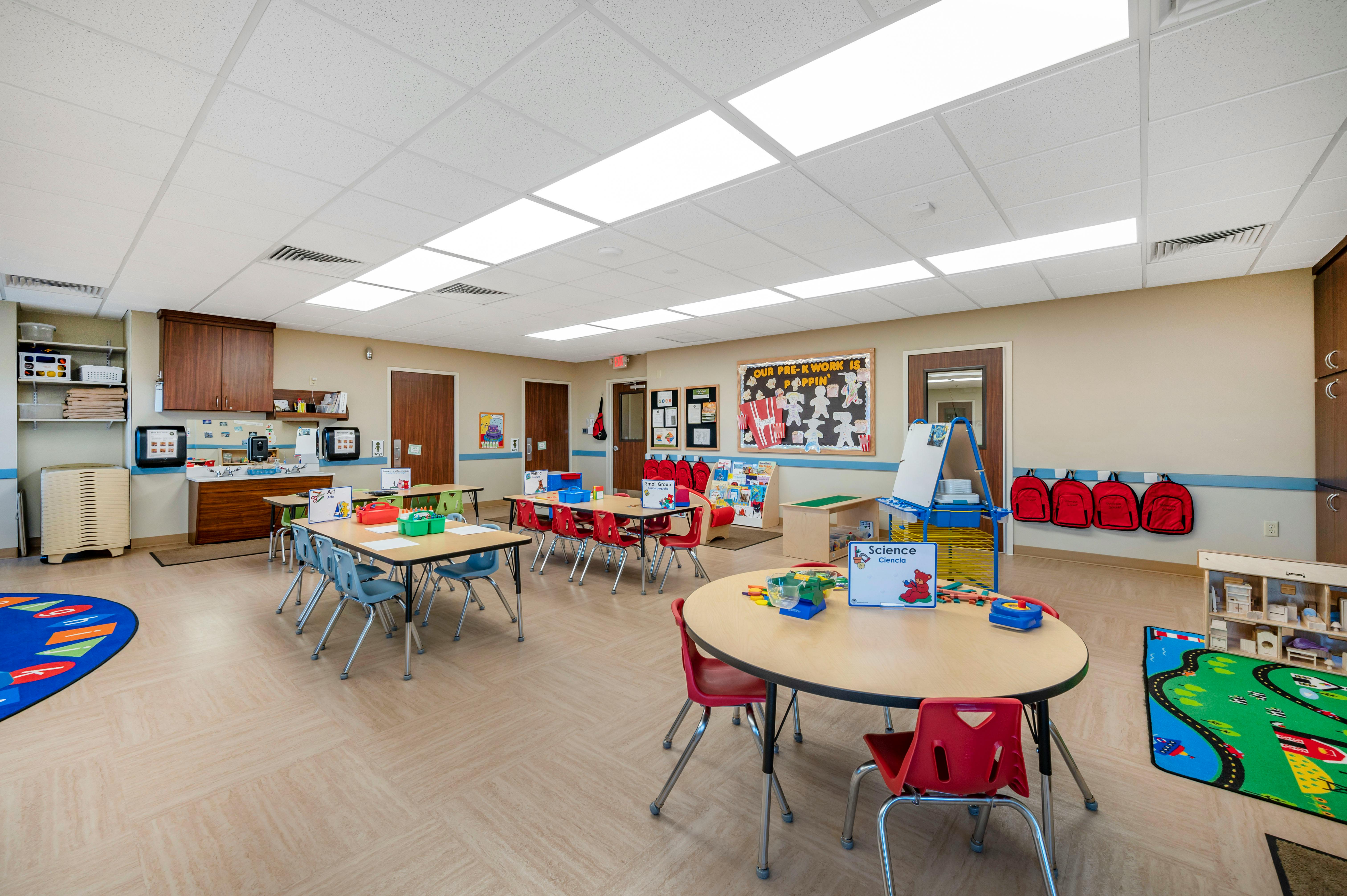 An empty classroom with small tables and chairs arranged, art supplies, and a science station