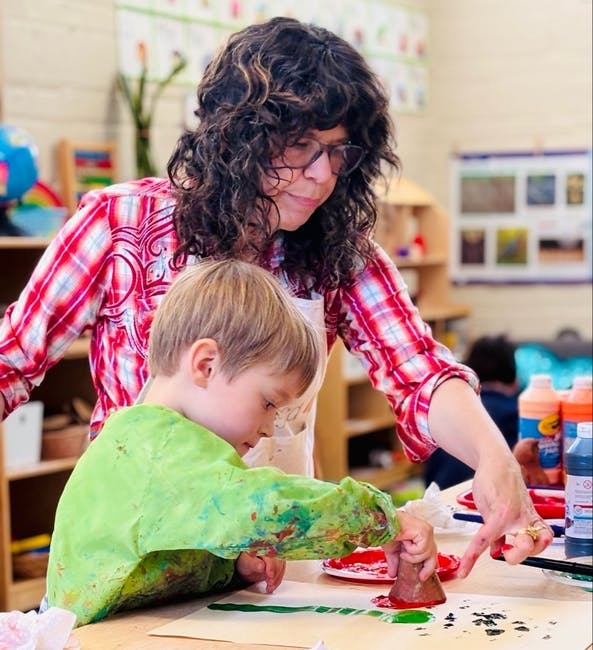 Adult assisting a child with a potato stamp painting activity in a classroom