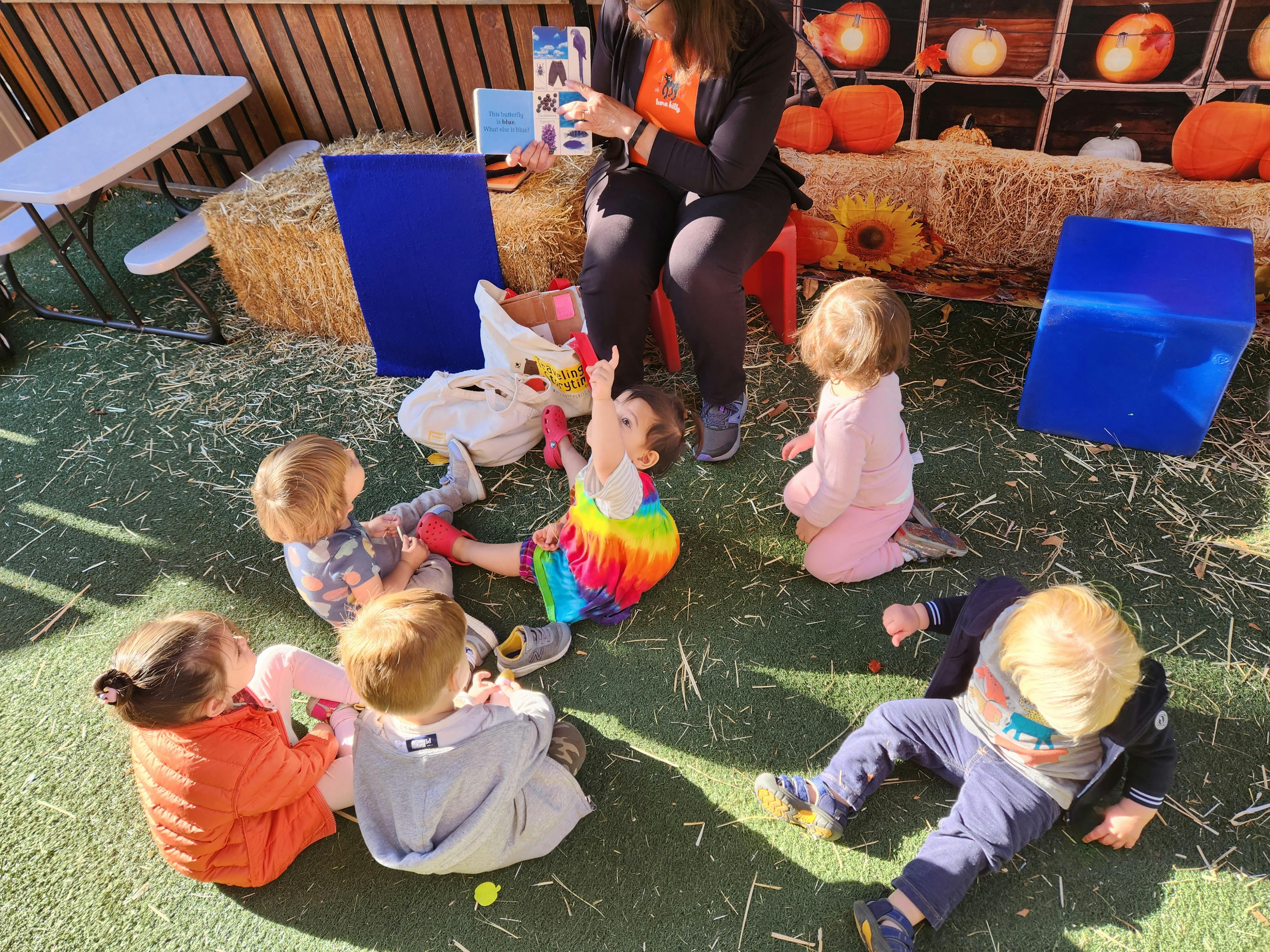 Adult reading a book to a group of children sitting on the ground