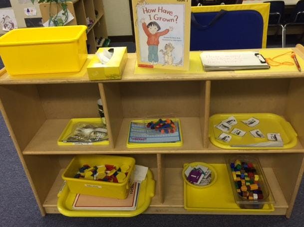 Wooden shelf with yellow bins, trays, and a children's book