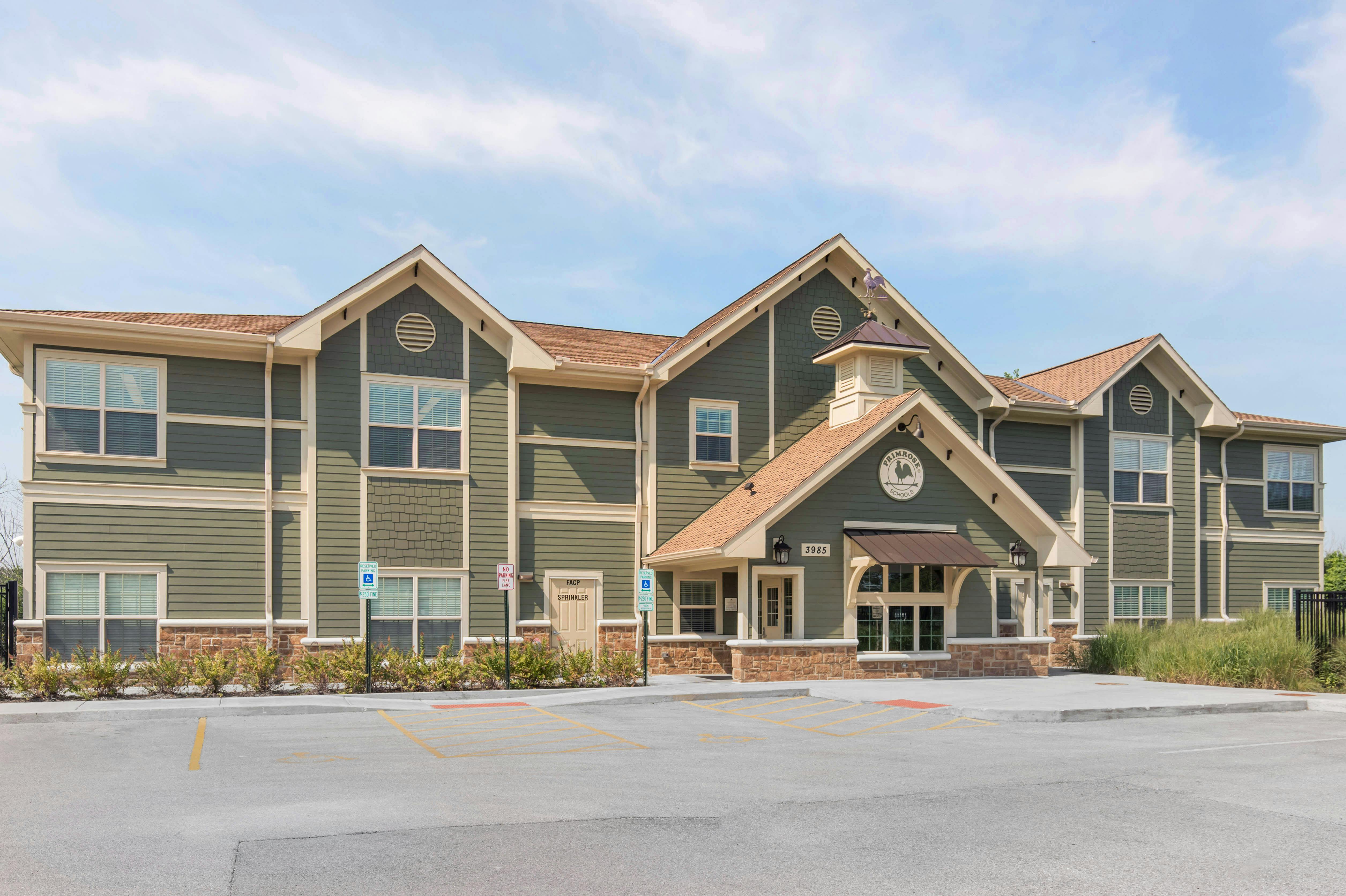 A multi-story building with green siding and brown roof, a sign says Primrose Schools