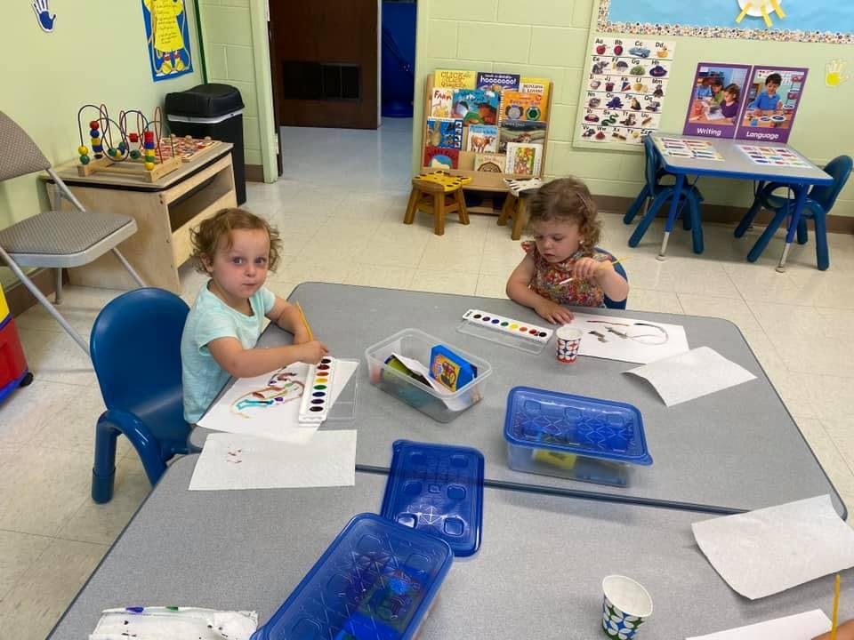 Two children sitting at a table with art supplies
