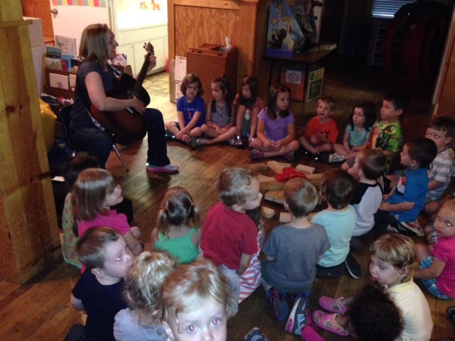 Person playing guitar for a group of children sitting on the floor