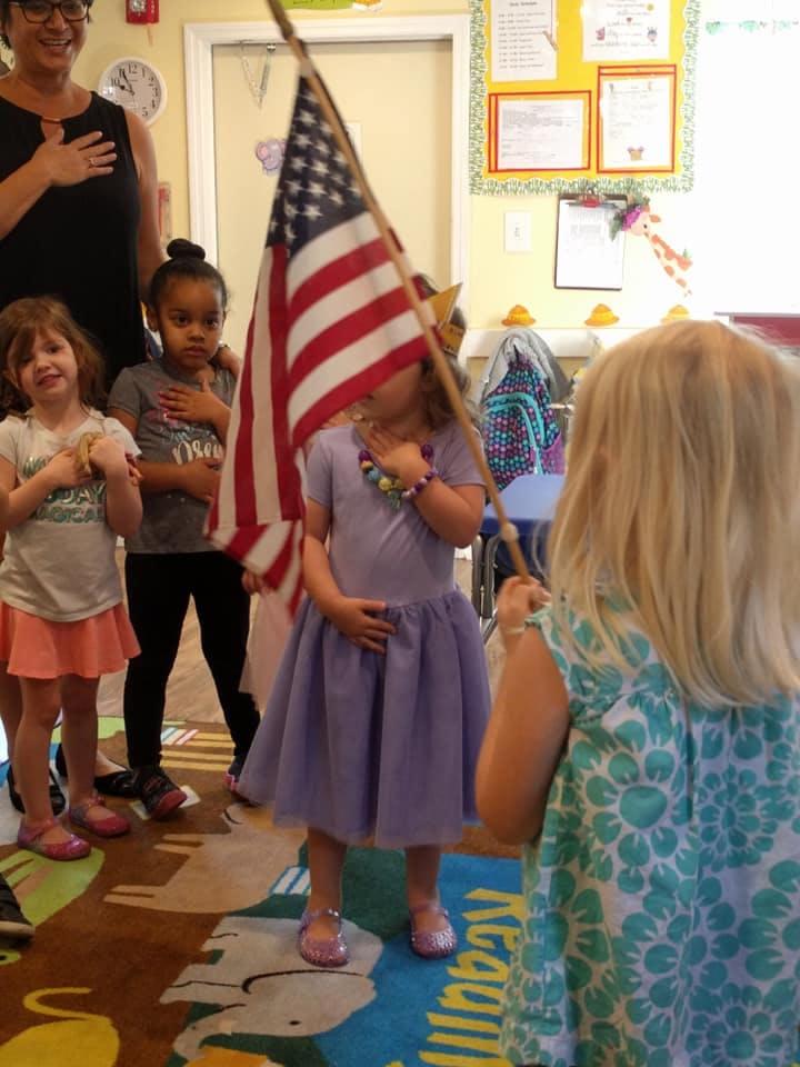 Children with hands over hearts during a pledge, one holding an American flag