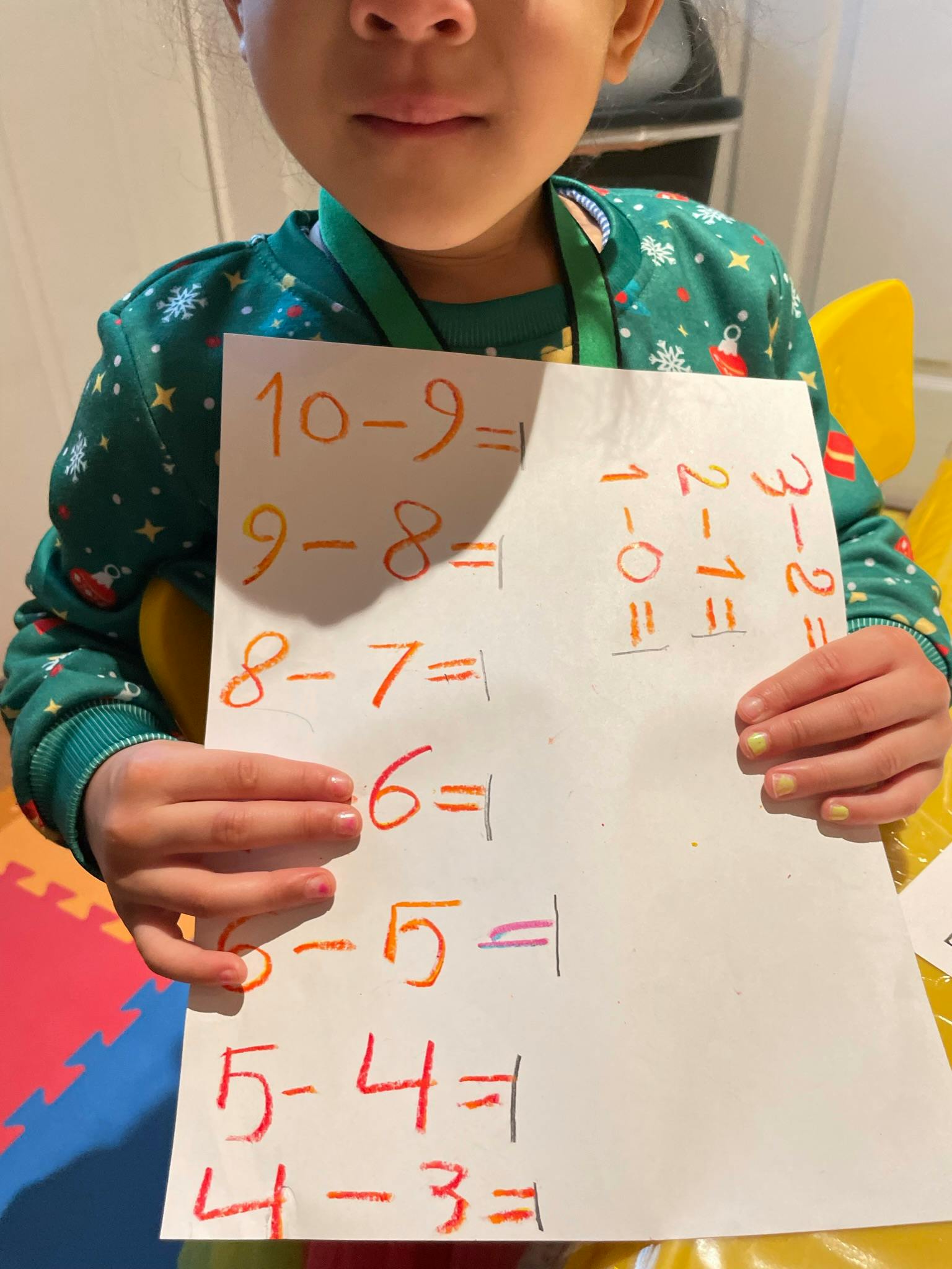 Child holding a paper with subtraction problems written on it