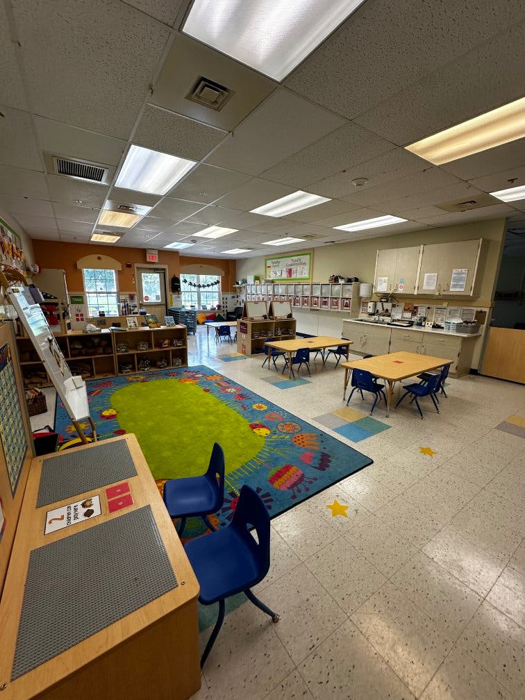 Empty classroom with tables, chairs, a rug, and windows