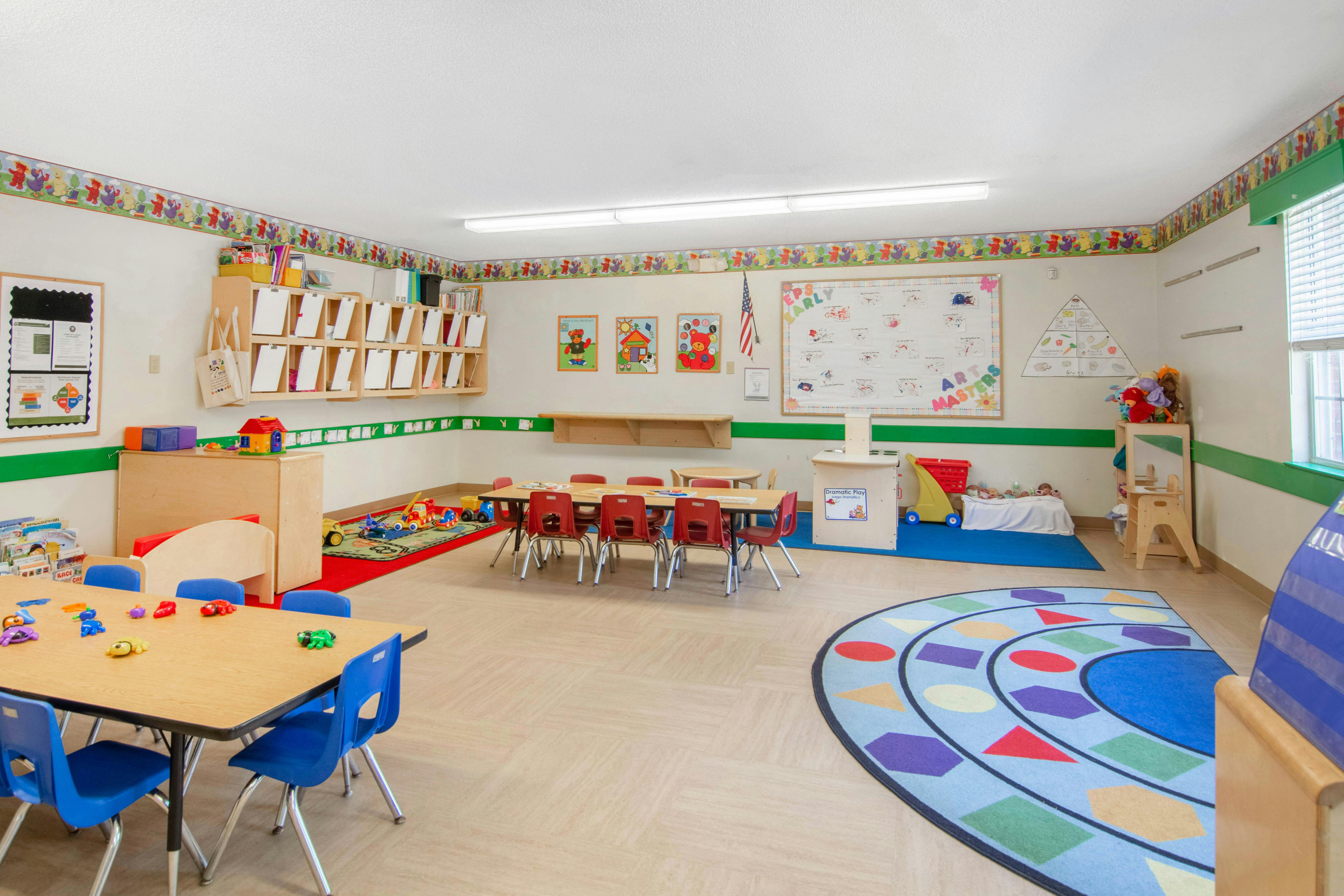 Classroom with child-sized tables and chairs, toys, and educational posters on the walls