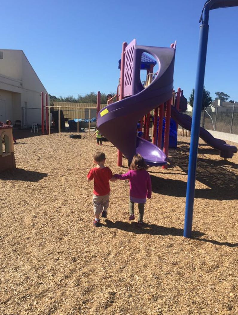 Two children walking on a playground toward a slide