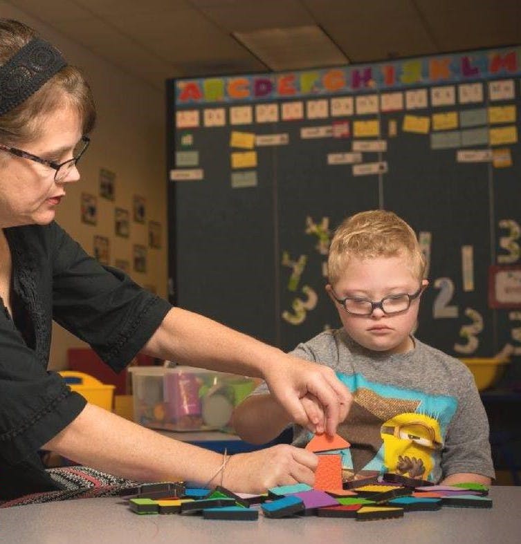 Adult and child playing with colorful geometric shapes at a table