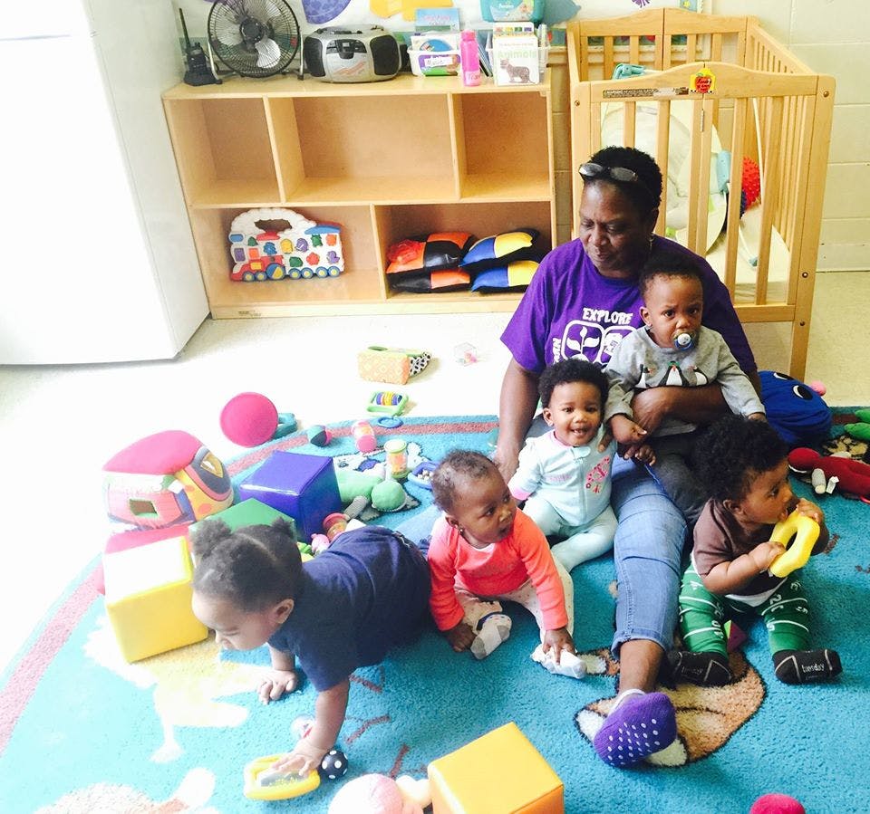 Person sitting on floor with multiple children playing around them