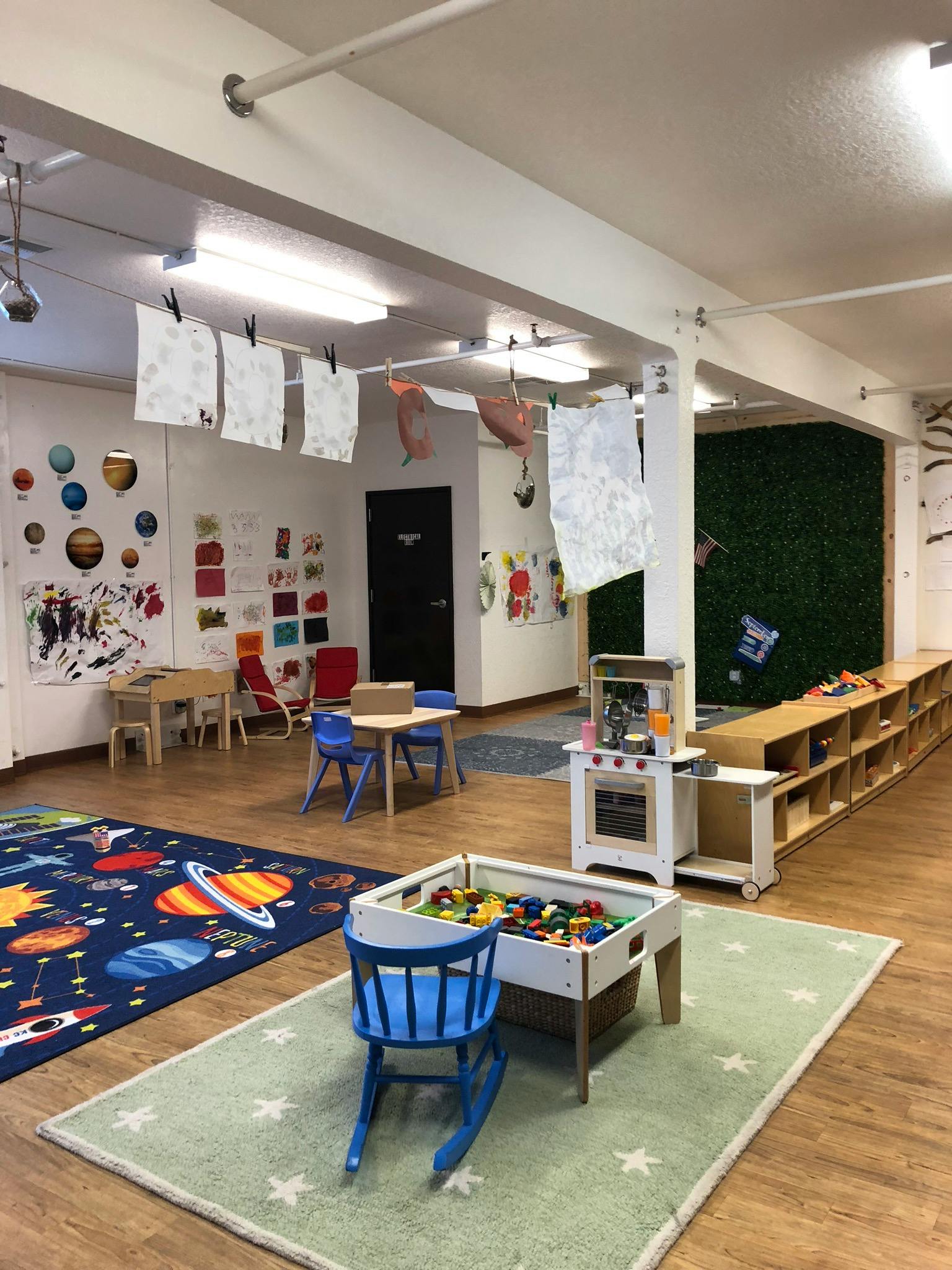 A classroom with play areas, small tables and chairs, and artwork on the walls