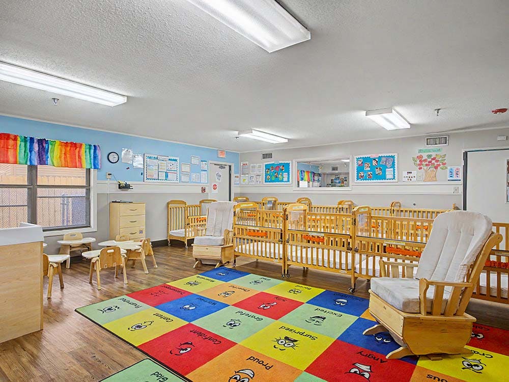 An empty nursery with multiple cribs, a colorful rug, and child-sized furniture