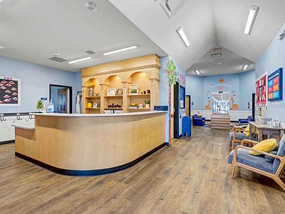 Reception area with a light wooden desk, shelves, and seating in a childcare center