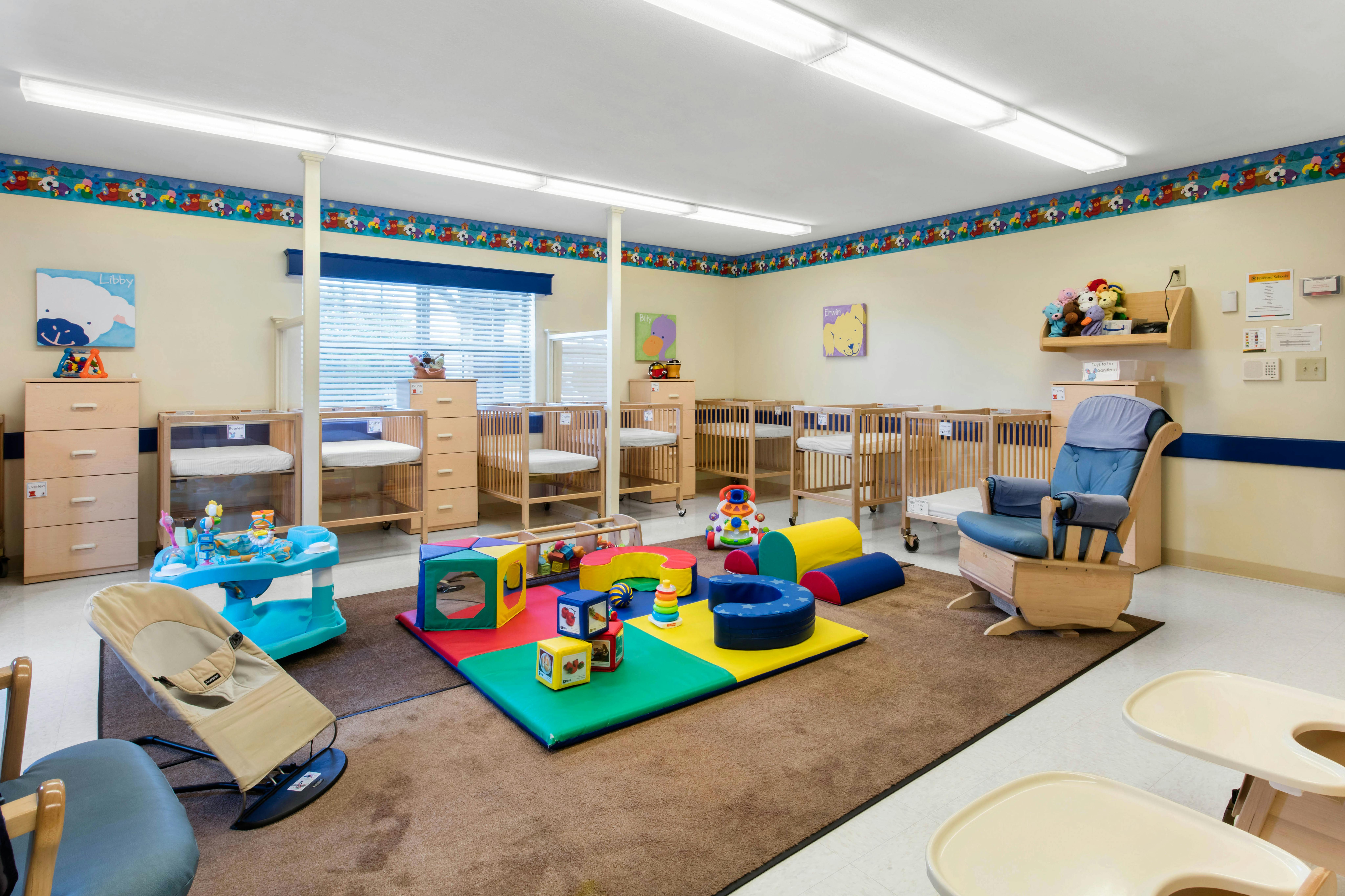 Baby room with multiple cribs, a play mat with colorful toys, and a rocking chair