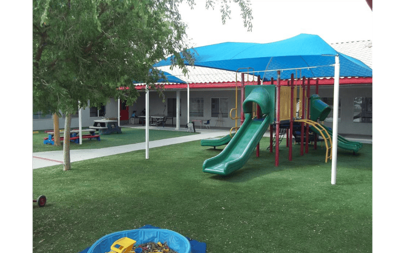 Playground with green slides, a blue shade canopy, and artificial grass