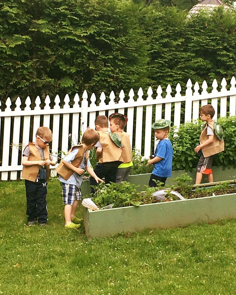 Children in vests looking at plants in a raised garden bed