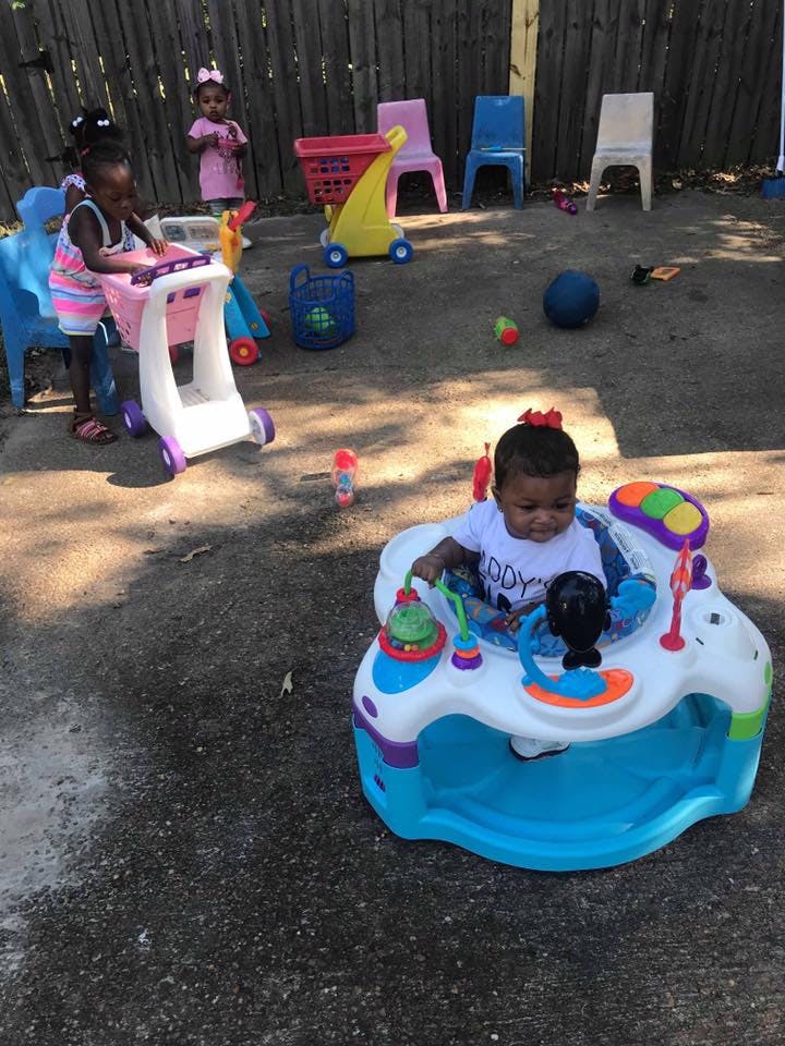 Child in a baby activity center, another child pushing a toy shopping cart