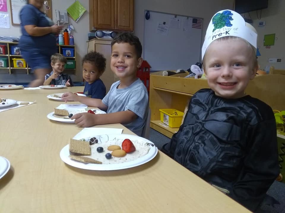 Children sitting at a table with plates of food in a classroom