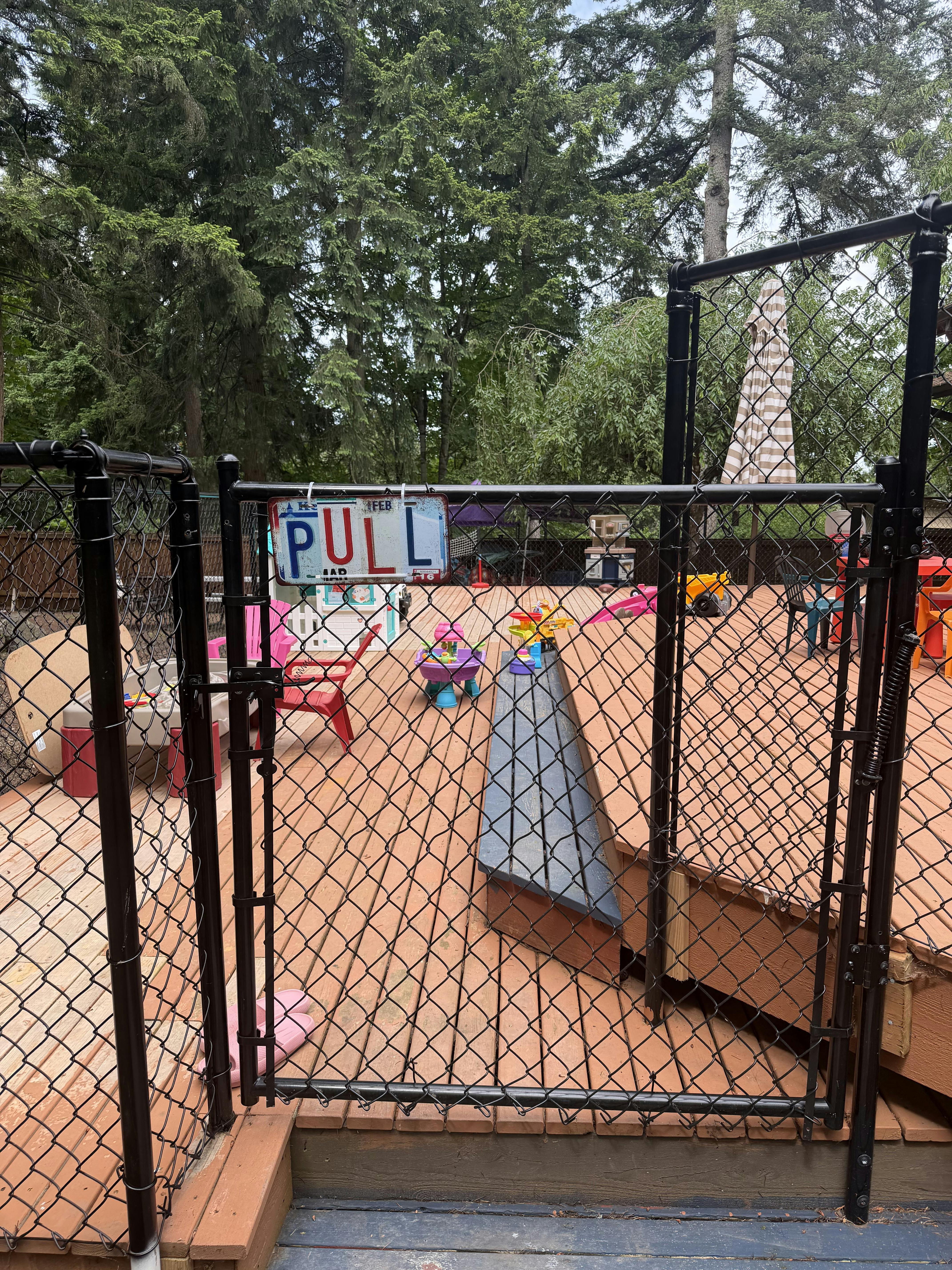 Chain link gate with a Pull sign opening onto a wooden deck with toys