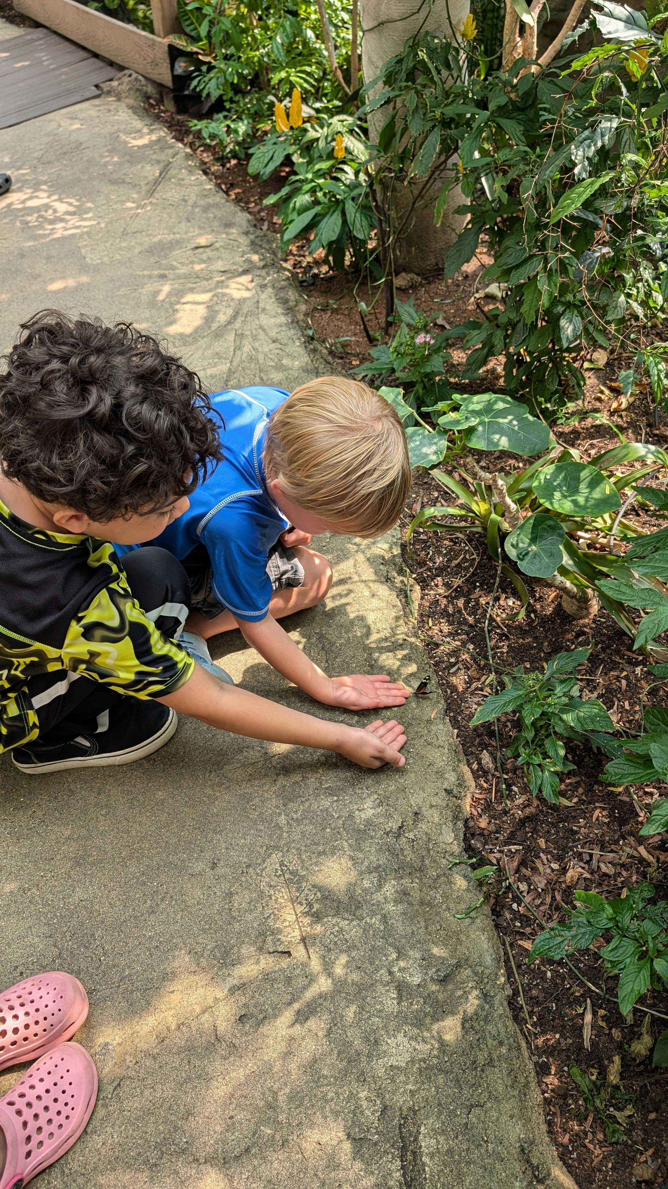 Two children kneeling on a path, looking at something on the ground