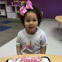 Child with a pink bow and unicorn shirt sitting in front of a cake