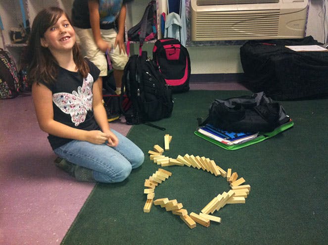 Child kneeling on floor next to dominoes arranged in a heart shape