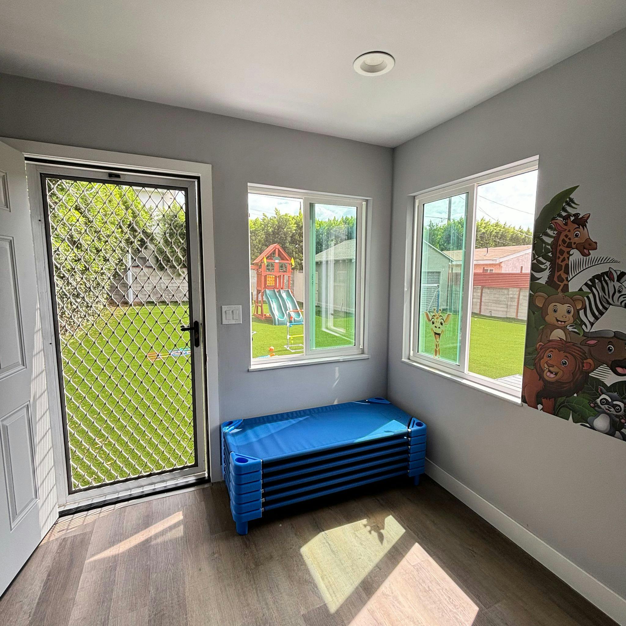 Classroom with blue cots, windows overlooking a playground, and animal wall decals