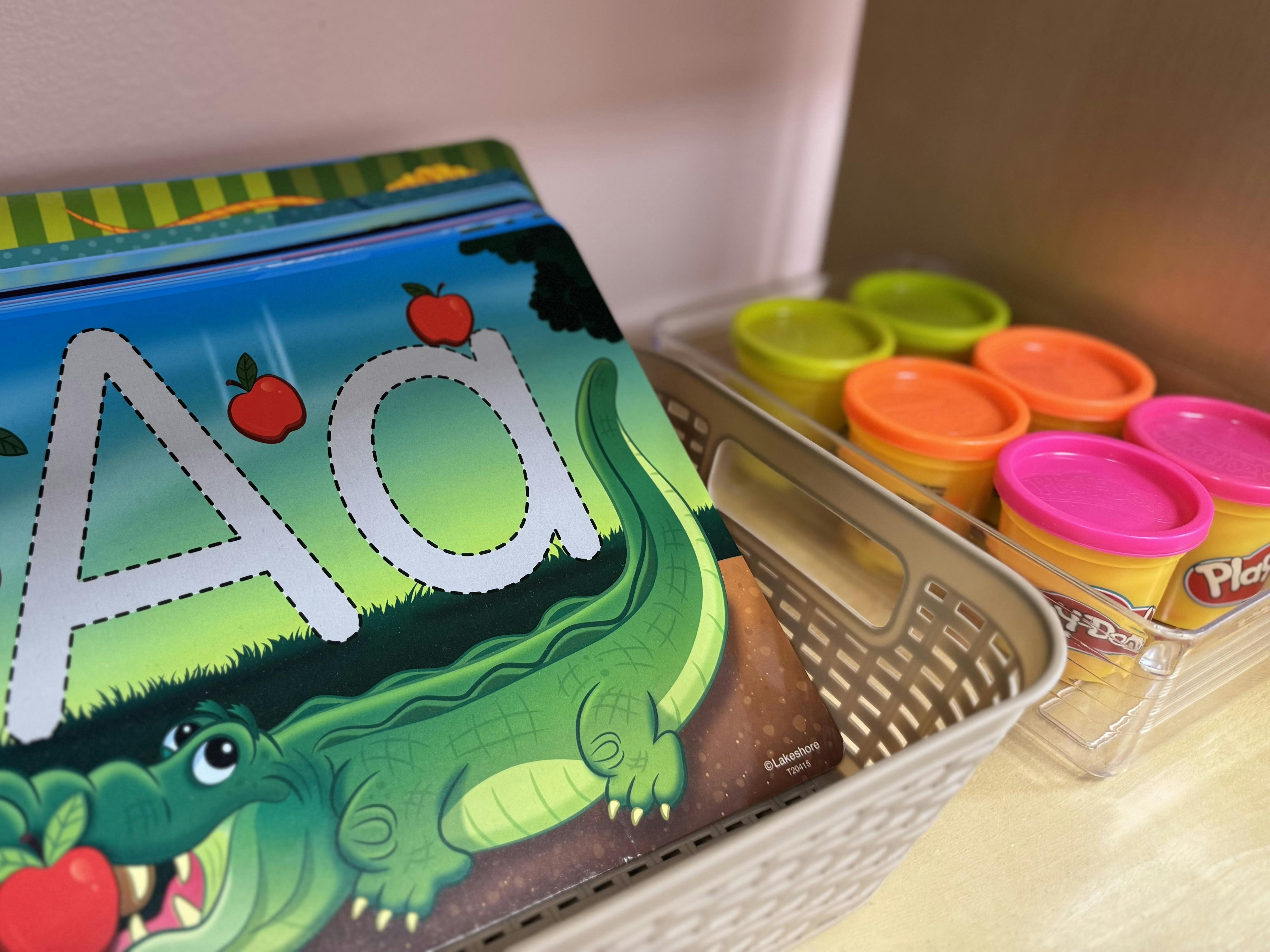 Children's book with alligator and letter A next to Play-Doh containers