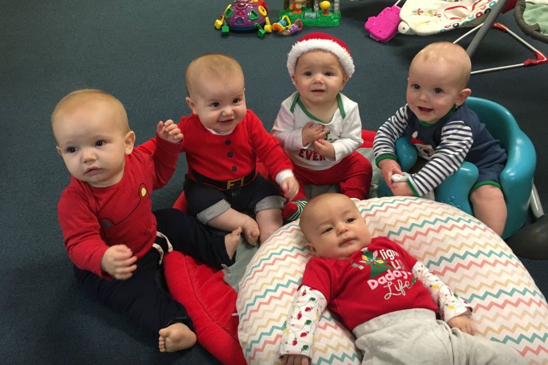 Five babies in red and white clothing sitting on the floor