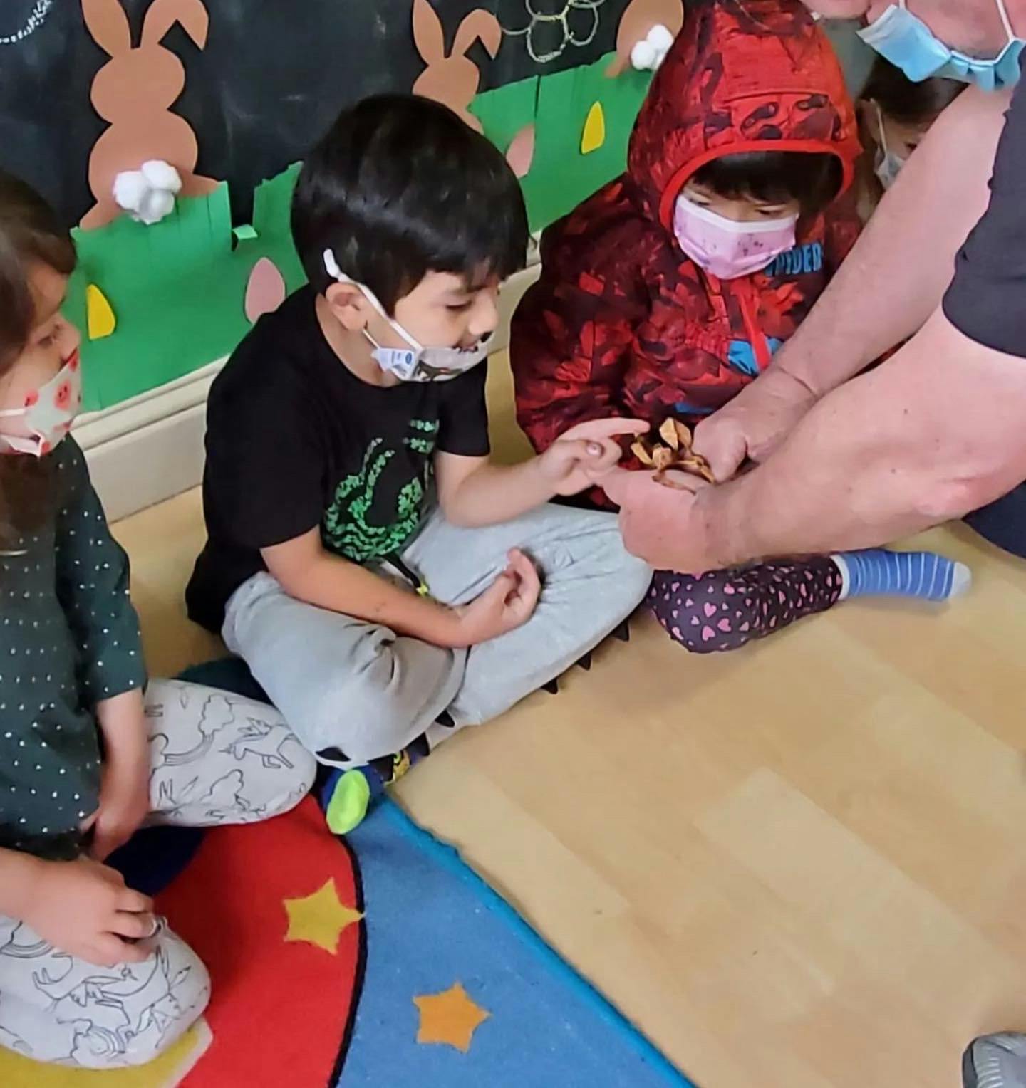 Adult showing small objects to children wearing masks
