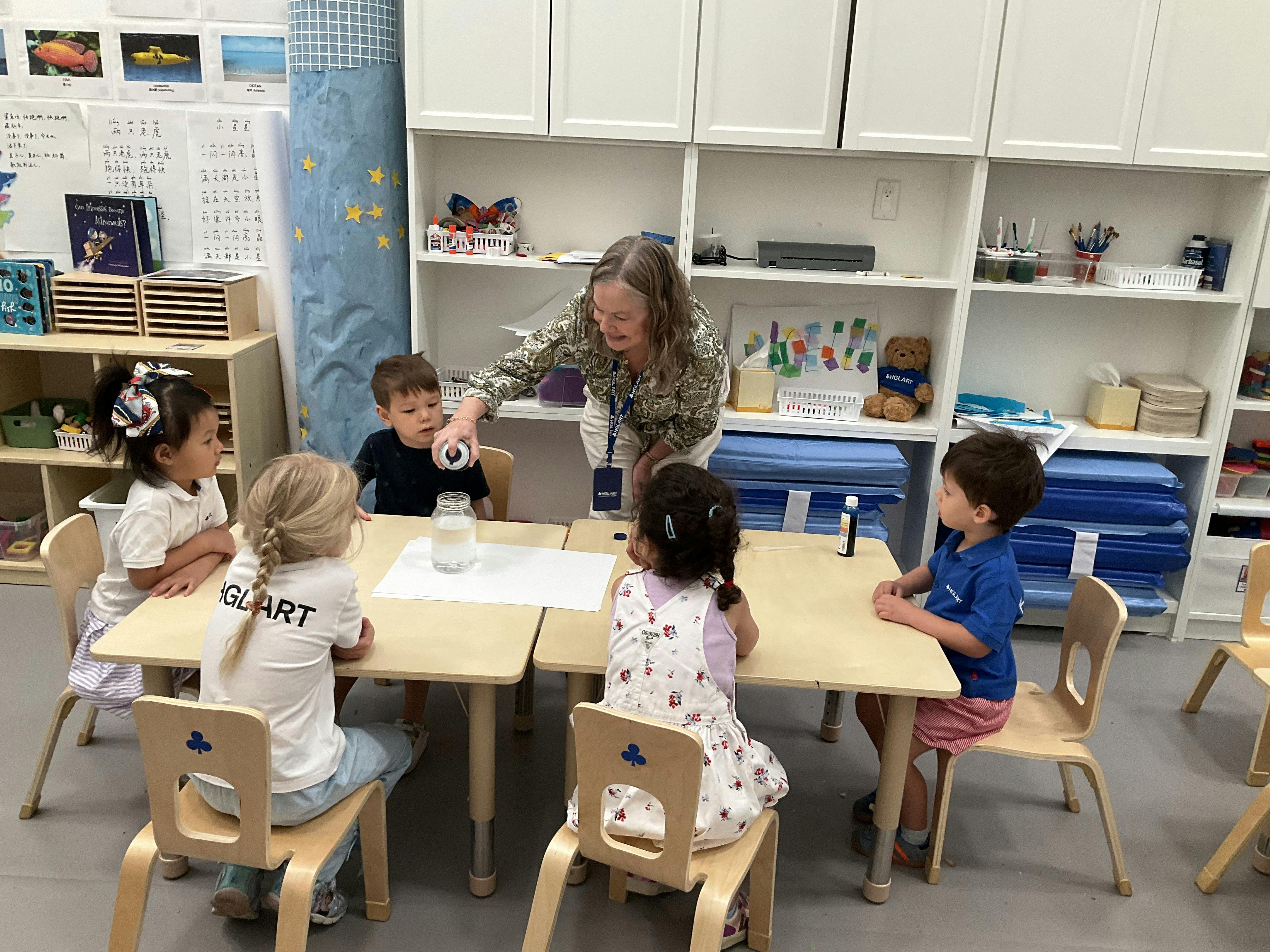 Adult and four children at small tables in a classroom