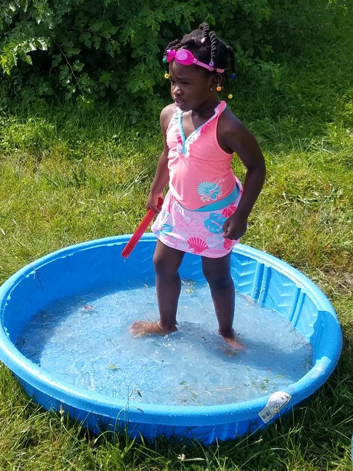 Child in a pink swimsuit standing in a blue kiddie pool