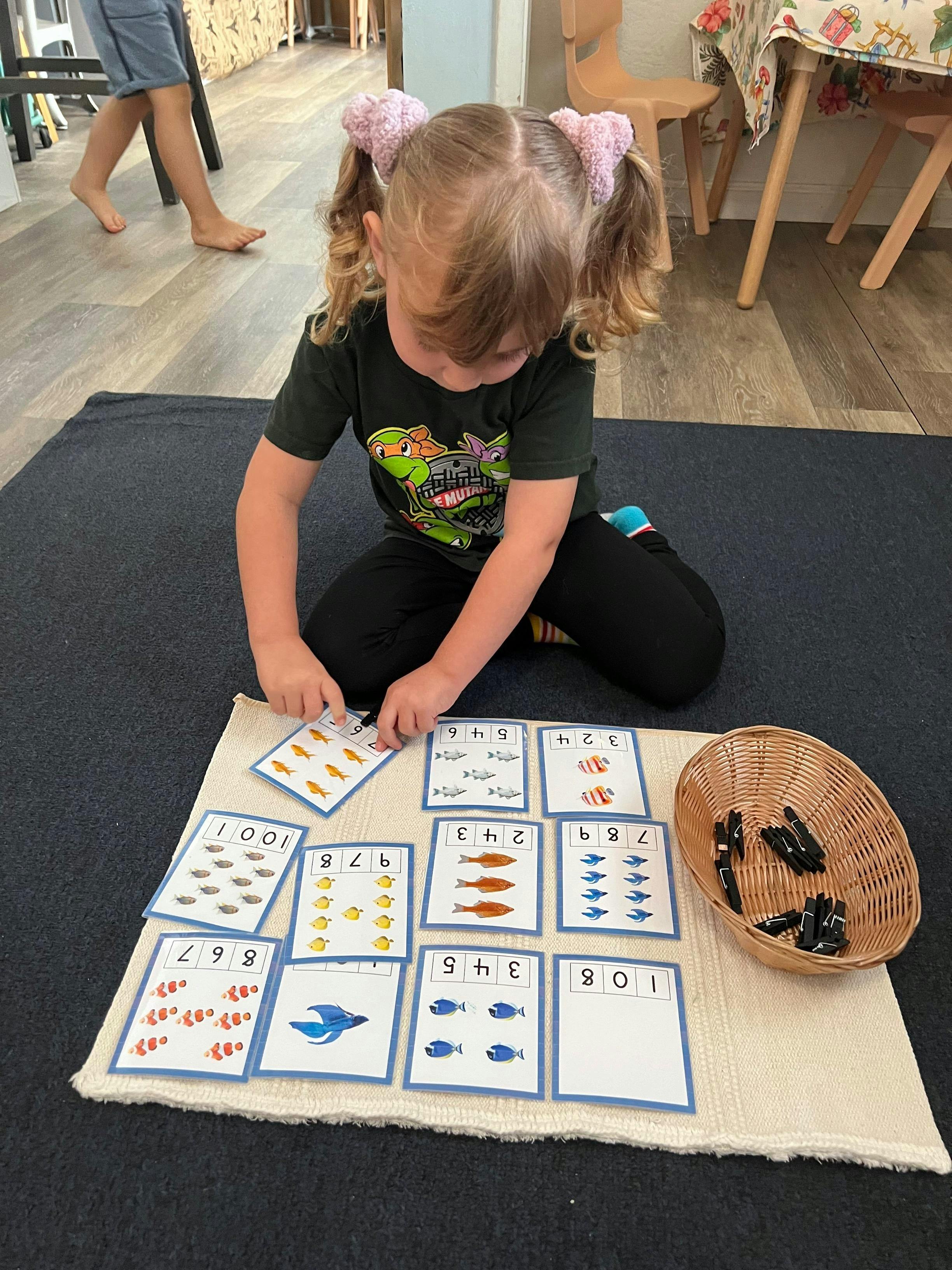 Child on floor playing with cards featuring fish and numbers