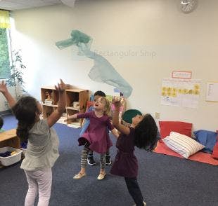Children playing with a light blue fabric in a room