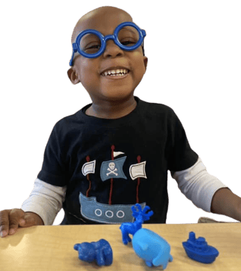 Child wearing blue glasses and a pirate ship shirt with blue toys on a table